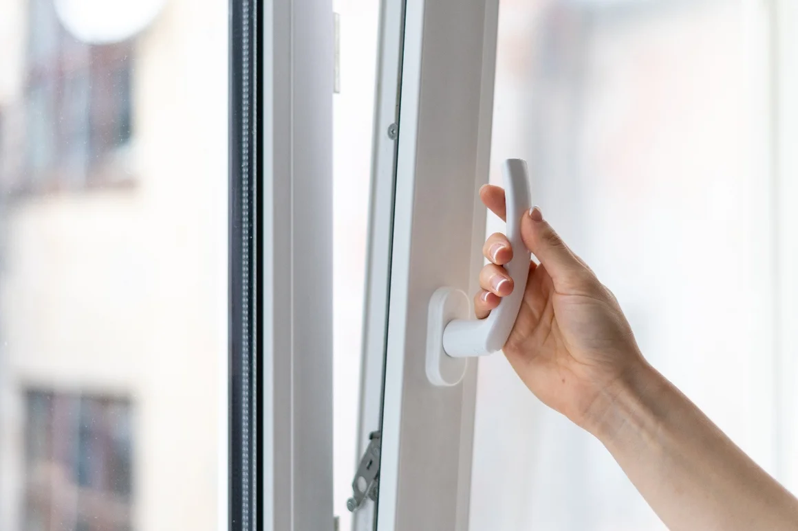 Hand öffnet Fenster mit weißem Fenstergriff